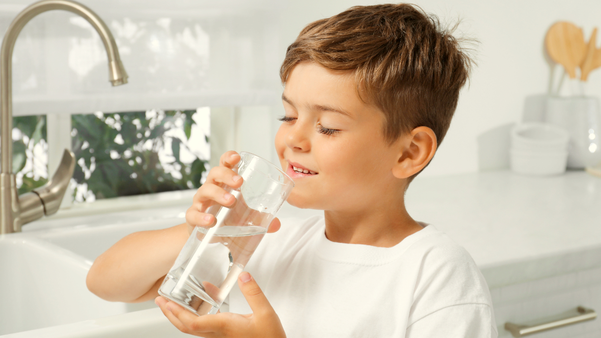 A young boy drinking a glass of water in the kitchen, illustrating the link between hydration and cognitive performance. Cleartide bottleless water in Boston supports children's hydration needs.