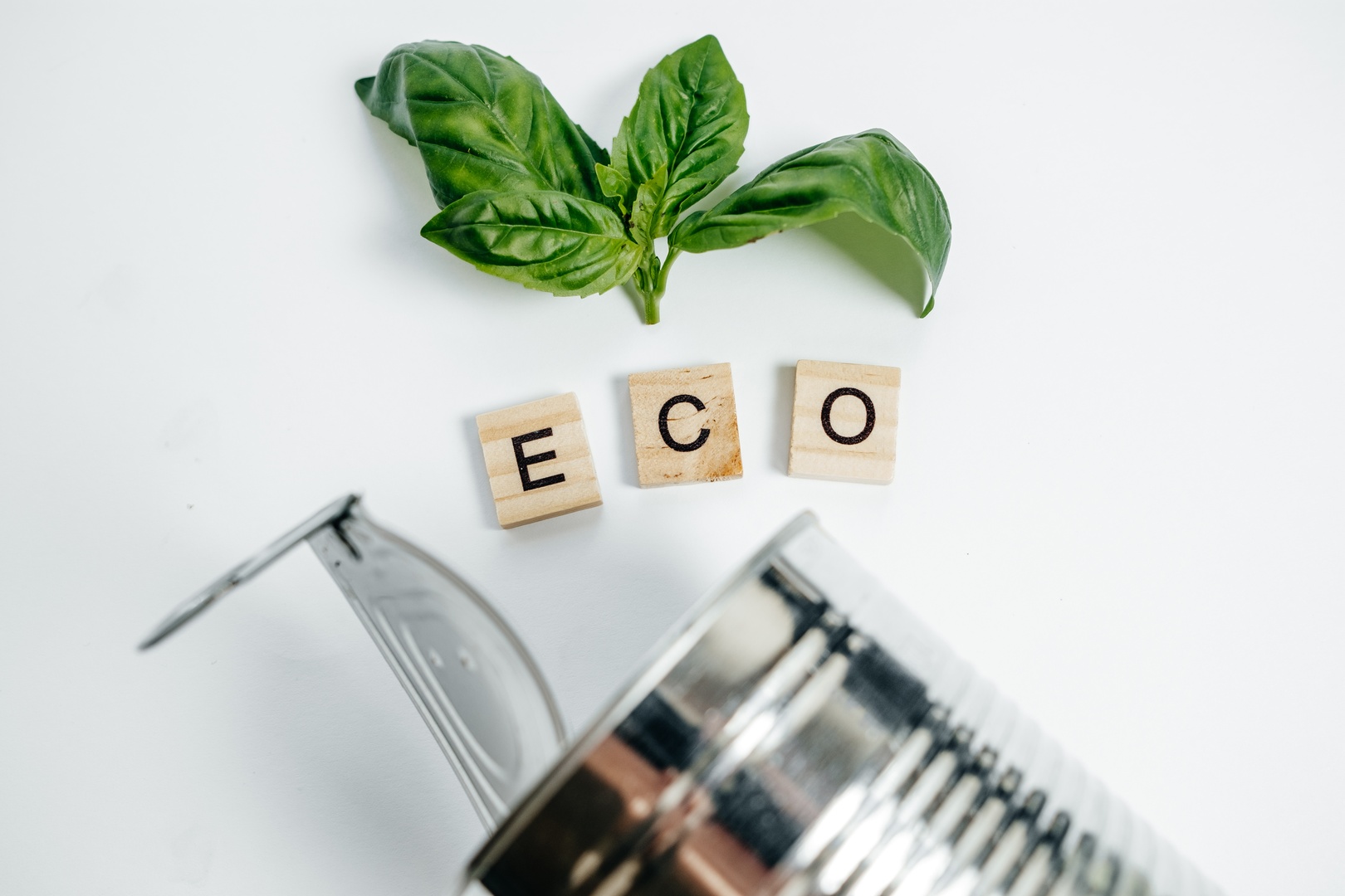 Eco-friendly concept with fresh basil leaves, 'ECO' spelled on wooden tiles, and a metal can, emphasizing sustainability and Cleartide's solutions.