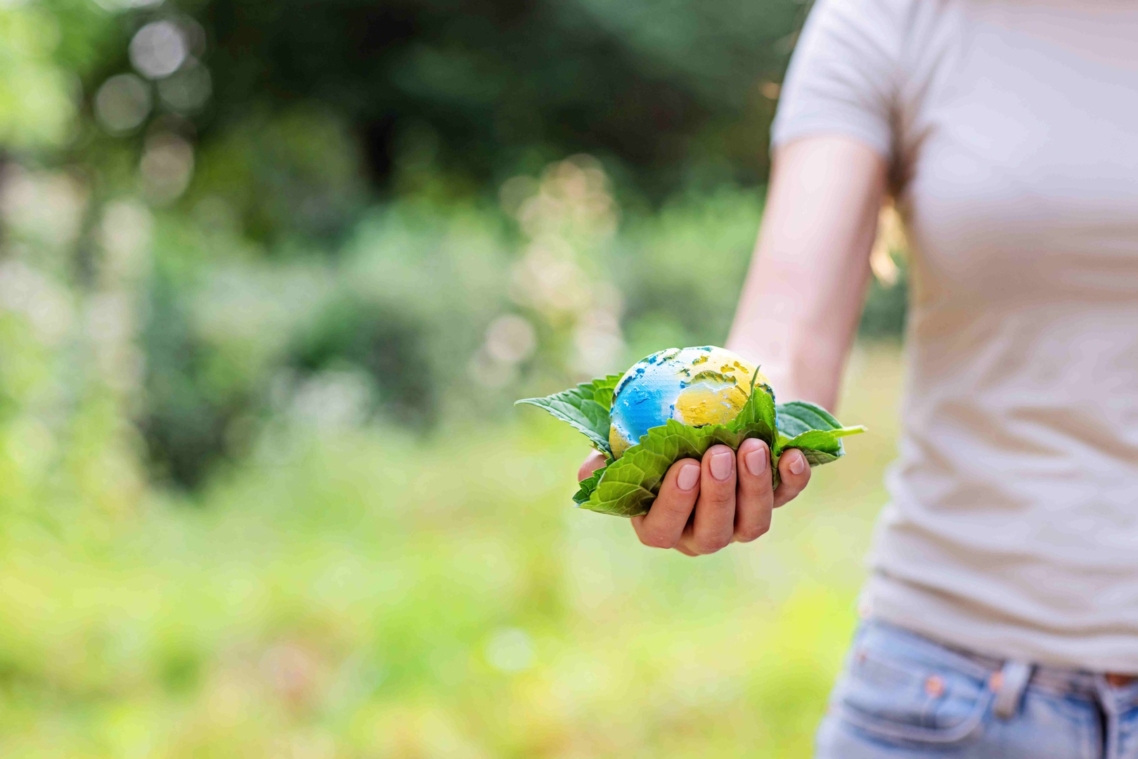 Person holding a small globe wrapped in green leaves, symbolizing eco-friendly practices and the economic benefits of Cleartide's sustainable solutions.